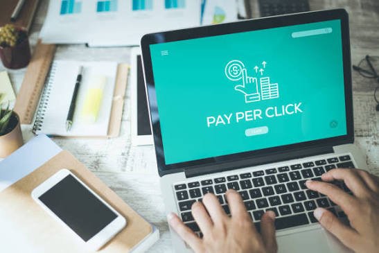 Laptop screen displaying a Pay Per Click icon while someone types