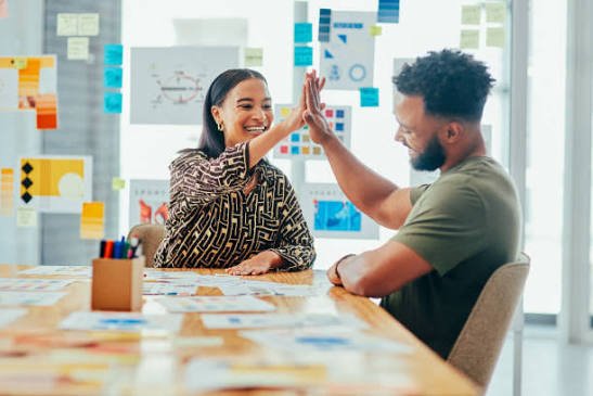 Two coworkers high fiving in front of a wall of brand mood boards
