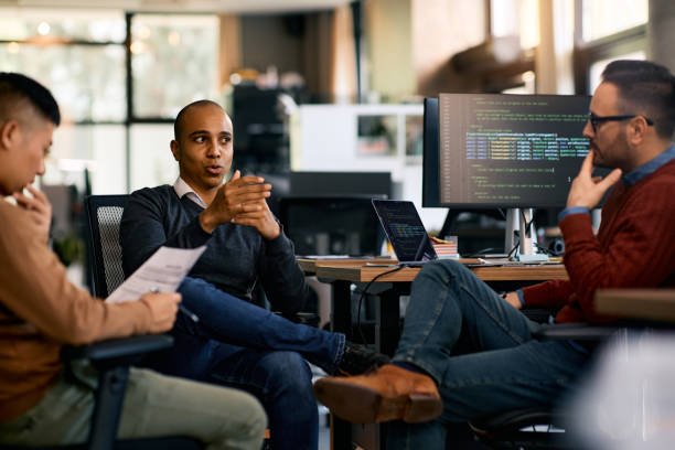 Web design team discussing a project with code visible on a monitor